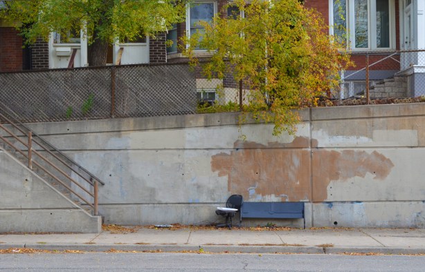 an old office chair beside a bench on the sidewalk 