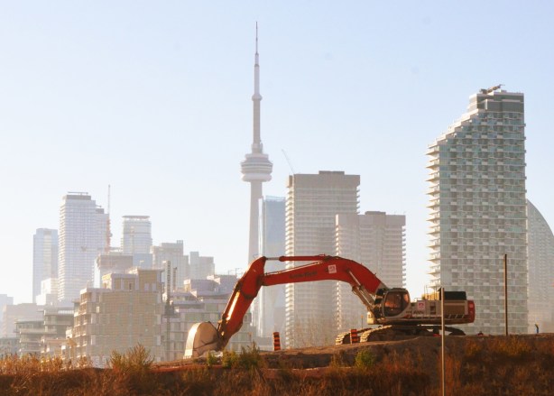 in the foreground, a red digger digs soil in the port lands, the CN Tower and toronto skyline in the distance 