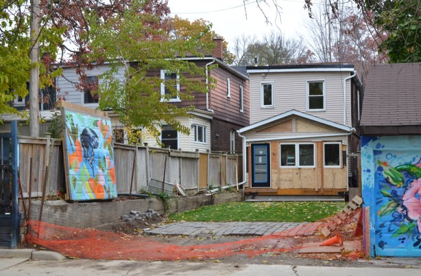 a house, seen from the back, being renovated, backyard is also being fixed up, fence between house and park has been removed, but garage door with mural on it has been preserved 