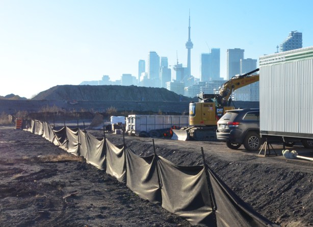 draped black fabric forms a fence at a construction site, CN Tower and Toronto skyline in the distance