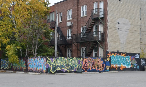 fence covered with throwups and wildstyle around a low rise apartment building