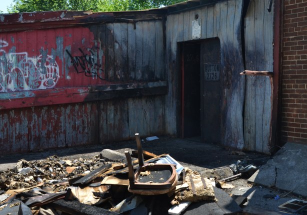 rubble, the result of a fire, sits in a pile behind a store in an alley, part of a chair sits on top 