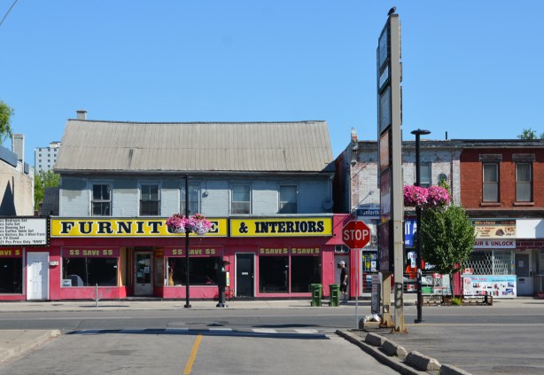 furniture store in old two storey building on the Danforth   with three big windows with save $ $ signs, old building with sagging roof. 