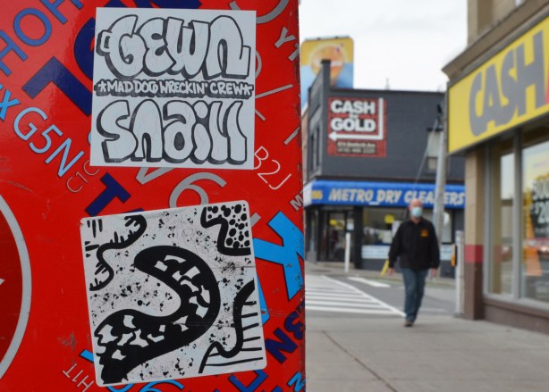 2 graffiti stickers on a Canada Post box, the top ones says gewn snail, the bottom one is an abstract drawing in black and white 