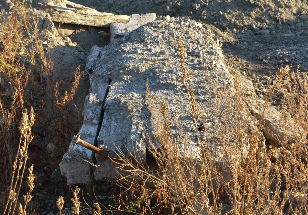 giant spike sticking out of an old piece of wood,dirty, on ground, in construction zone 