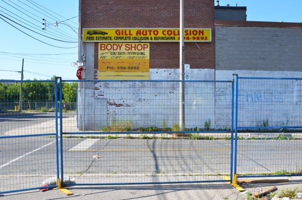 blue metal construction fence, empty parking lot beside building with a sign on it that says Gill Auto Collision
