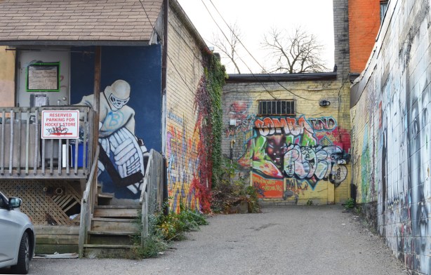mural of hockey goalie on the back porch of the hockey store, other murals on the buildings beside, including one that says bomba end 