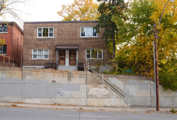 square, two storey brick duplex on a hill, with concrete wall in front, lots of steps going up 