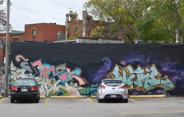 two cars parked in front of a kizmet mural 