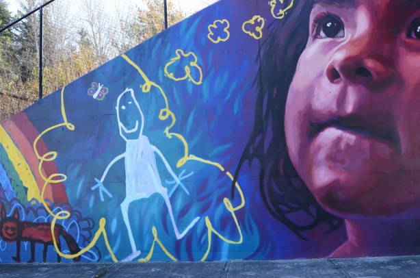 part of a mural by Lacey and Layla called Colour Outside the Lines, a young girl looking upward, a child's drawing of a girl in with a curly yellow line around it 
