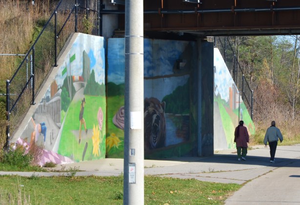 two people walk past a mural on a railway underpass