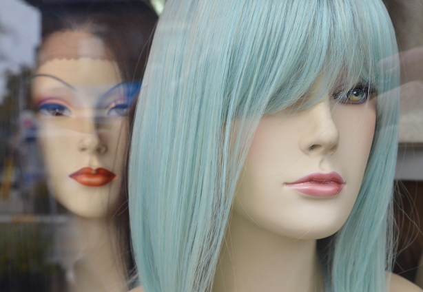 two wig mannequin heads in a store window. the one in front has pale turquoise hair, the one in the back has black hair.