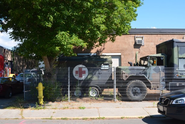 old drab green military truck and ambulance with red cross symbol parked in front of a building
