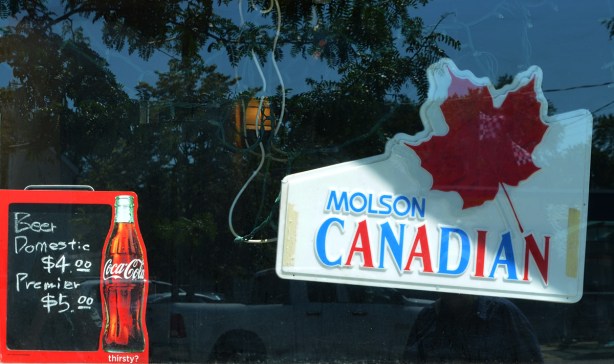 bar window, with Molson Canadian advert with red maple leaf, also coca cola sign with beer prices listed 