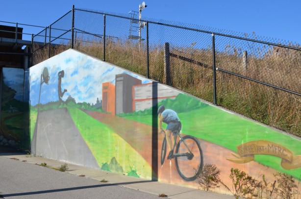 old mural on concrete wall, of a person on a bike on a path, someone playing basketball, in the mural, 