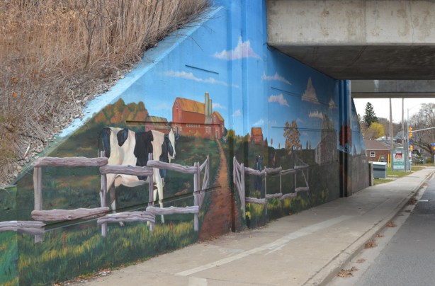 cow, farmyard scene in a mural, beside sidewalk on railway underpass
