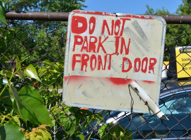 hand painted sign on a chain link gate that says do not park in front door 