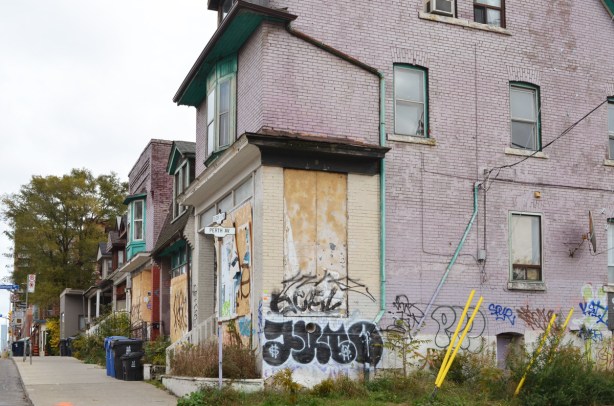 pale purple brick building boarded up, plywood on windows, yard overgrown, 