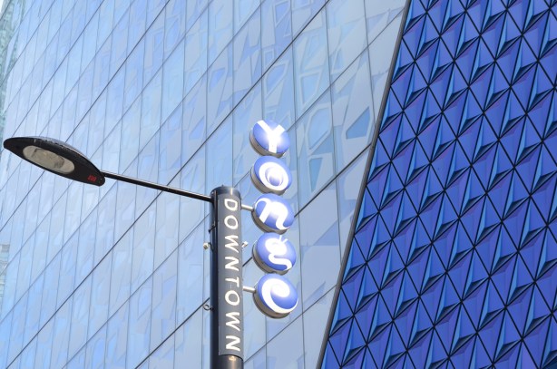 blue glass on the exterior of Ryerson student building, with a downtown yonge sign on a street light beside the building 