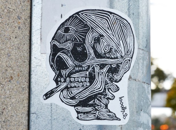 sticker graffiti of a head without the skin, showing eye socket, muscles, teeth, top vertebrae, smoking a cigarette 