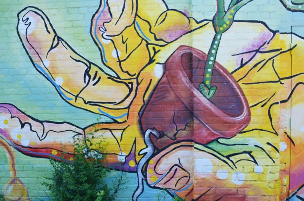 hand holding a flower pot that is cracked because the root of the plant is growing, in a mural