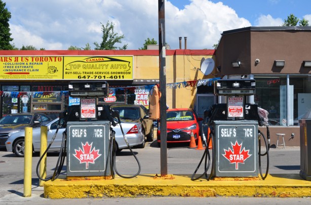 gas station, two pumps, star self service gas, cars parked behind at auto mechanic shop, top quality auto and cars r us toronto, open sign