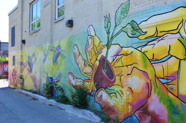 mural of a hand holding a plant growing in a flower pot, plus bees, 