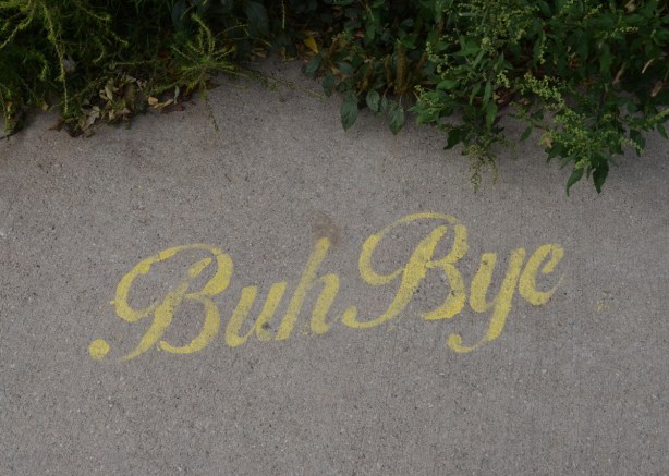 yellow stencil graffiti on sidewalk, words that say buh bye