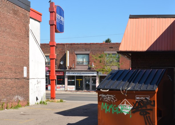 large sign on pole, stiches outlet, beside a driveway, stores across the street, divine photography