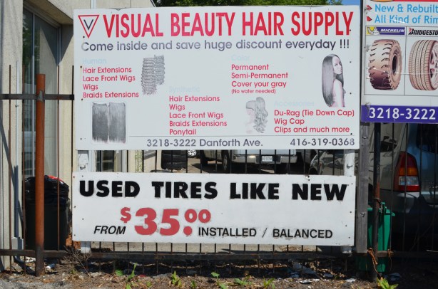 on a fence beside a store, advertising used tires for sale , like new, at thirty five dollars each. also a sign for visual beauty hair supply with a list of some of their products 