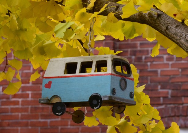 a small replica of a VW bus hanging from a tree. bus is painted white and blue and has a red heart on it 