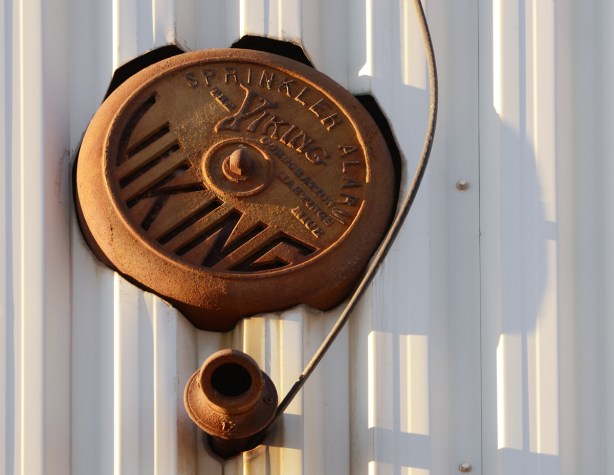 an old round rusty Viking brand sprinkler alarm on the outside of a building 