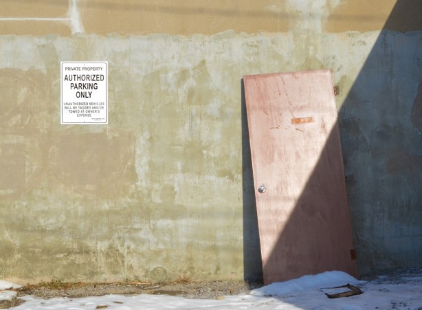 beige wall with diagonal shadow. Faded red door leaning against the wall (off hinges) so door is half covered by the shadow