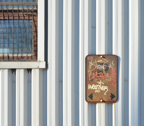corrugated metal cladding on a building with a window and an old rusty sign with graffiti on it 