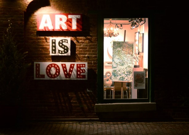 evening photo, distillery district, decorated for Christmas, the words art is love in big block letters, outside the window of an art gallery with a painting in the window 