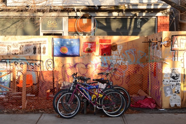 bikes locked in front of a plywood makeshift fence around an empty storefront at 86 Nassau street in Kensington, signs and graffiti on the fence, artwork, protest 