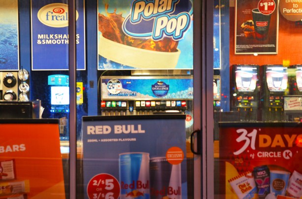 the window and glass door display of posters at a Circle K convenience store, in the evening, lights on, 