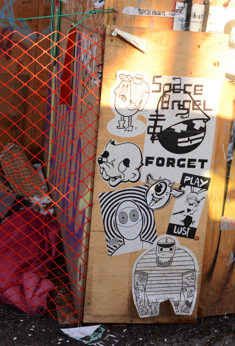 black and white posters and slaps graffiti on a plywood fence, urban ninja squadron, sketchrat, forget, 