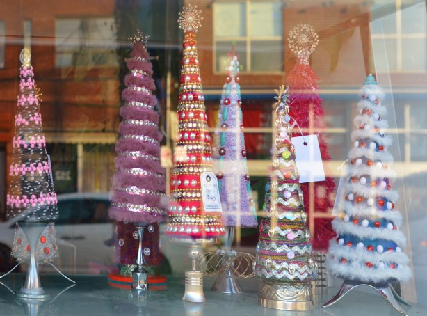 looking in a store window, little Christmas trees made in cone shapes with fuzzy and shiny items. 