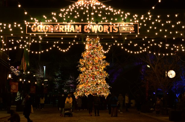 evening photo, distillery district, decorated for Christmas, large Christmas tree, sign Gooderham and worts over the road, strings of white lights 