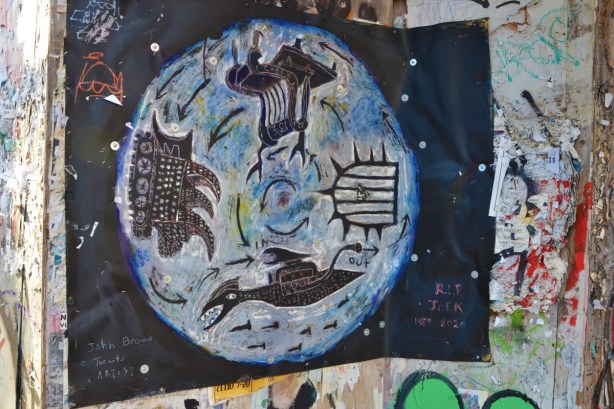 a painting tacked to construction hoardings, signed John Brown Toronto artist, on black paper, a circle with four main things inside it, first nations symbols 