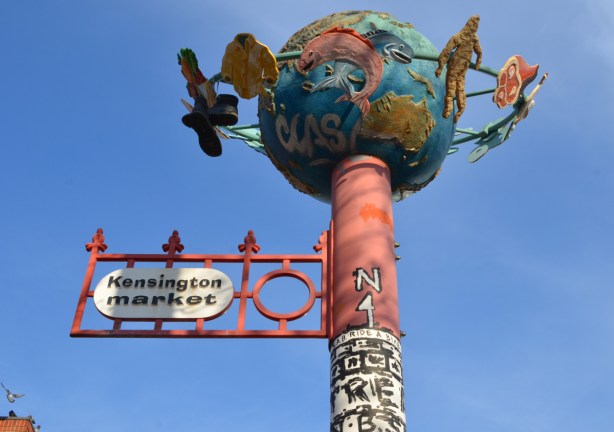 tall pole to mark Kensington market area of Toronto, with a globe on top. Circling the globe are objects like a shirt, a piece of meat, things that represent merchandise in the market
