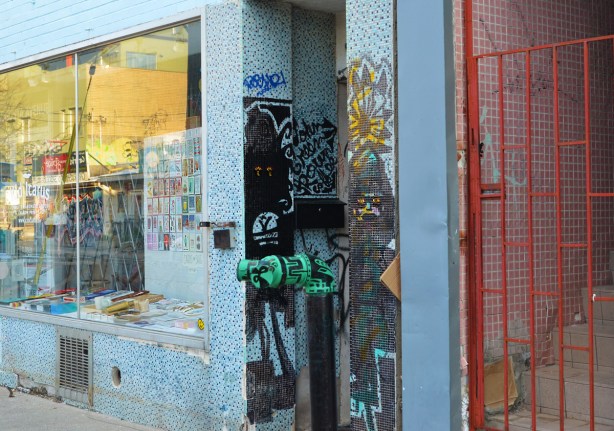store fronts & windows, small tiles on exterior wall, orange metal gate,, closed, with stairs behind it 