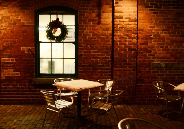 patio outside a restaurant window, wreath on window, snow on the table on the patio, metal table and chairs, old brick building in distillery district , 