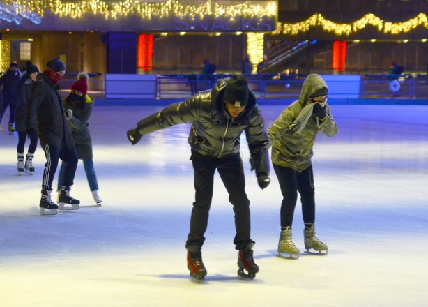 a young couple learning to skate together at Nathan Phillips, after dark, holding hands, hesitant but upright 