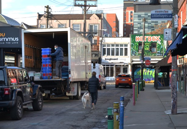 a man walks his dog along the street past the back of a truck where another man is unloading 