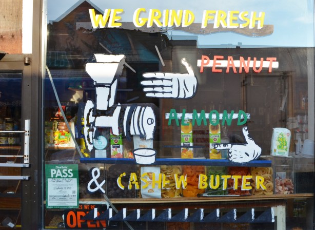 paintings on the glass on the window of a store, we grind fresh, peanuts, almonds, picture of a hand and a grinder 
