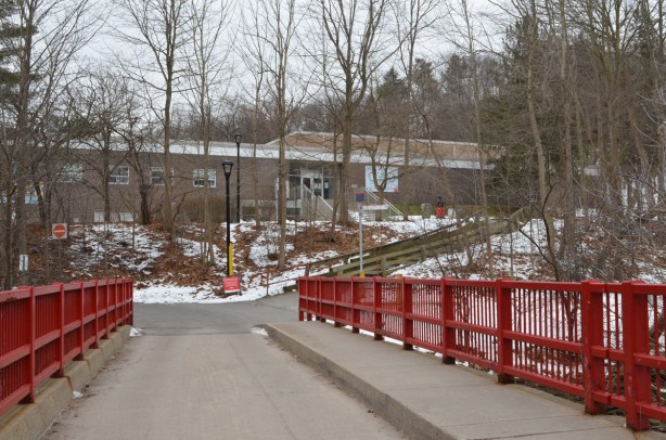 single lane bridge with wide sidewalk and bright red metal barricades on side, brick building in the background, trees, winter, 