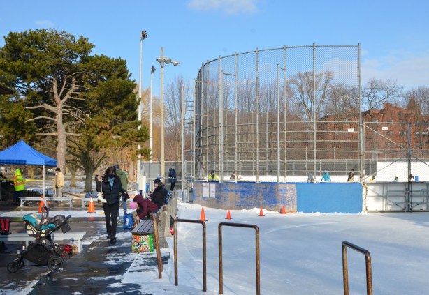 outdoor skating rinkm some people getting ready to skate, enclosed rink for hockey etc with more natural rink beside it 