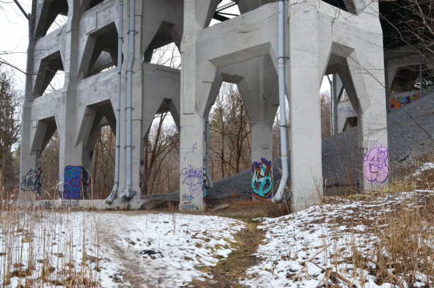 concrete pillars with some graffit on them, holding up a bridge, over snowy ground 